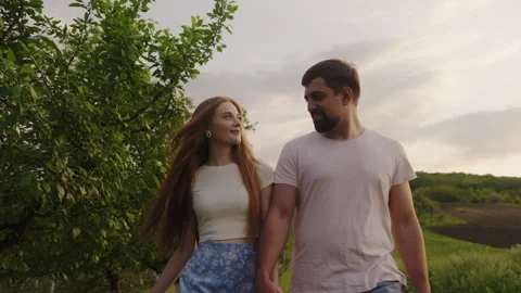 Front view of a young couple holding hands and walking through rural field 스톡 동영상 252249710