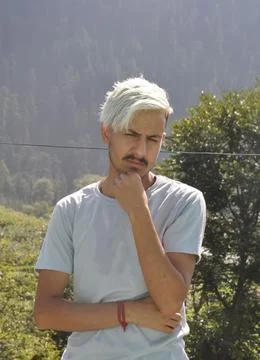 Front view of a young guy with dyed white hair posing with his hand on chin Stock Photos