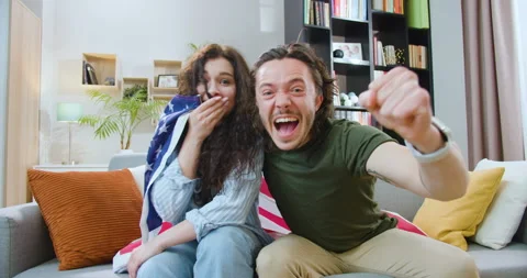 Front view of young man and woman covered with American flag sitting on sofa and Stock Footage 244139032
