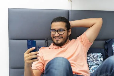 Front view of a young man in bed looking social media in his smart phone Stock Photos