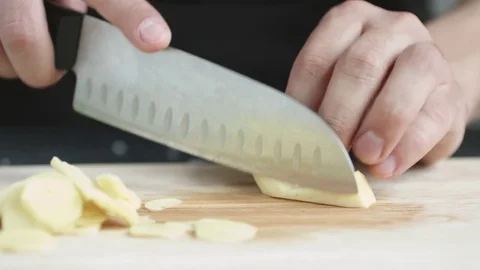 Front view of young man chef cut thin slices of a piece of ginger with knife on Stock Footage 74344409