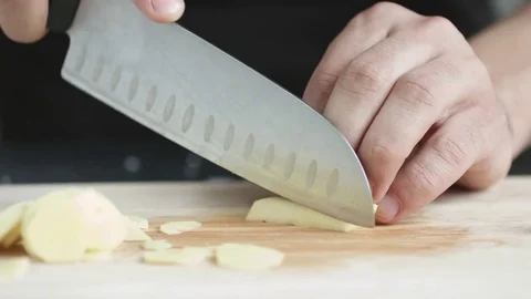 Front view of young man chef cut thin slices of a piece of ginger with knife on Stockbeeldmateriaal 74345185