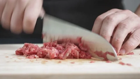 Front view of young man cook chopping piece of meat with knife on cutting board Stock Footage 74344610