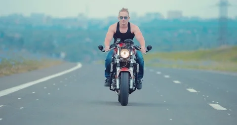 Front view of a young man in sunglasses riding a motorcycle on an asphalt road 스톡 동영상 92284000