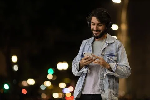 Front view of young man using a smartphone and headphones at night time with  Stock Photos