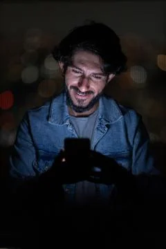 Front view of young man using a smartphone at night time with city view lands Stock Photos