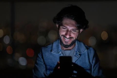 Front view of young man using a smartphone at night time with city view lands Stock Photos