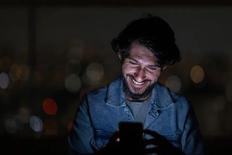 Front view of young man using a smartphone at night time with city view lands Stock Photos