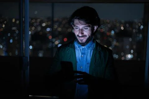 Front view of young man using a smartphone at night time with city view lands Stock Photos