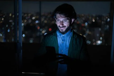 Front view of young man using a smartphone at night time with city view lands Stock Photos