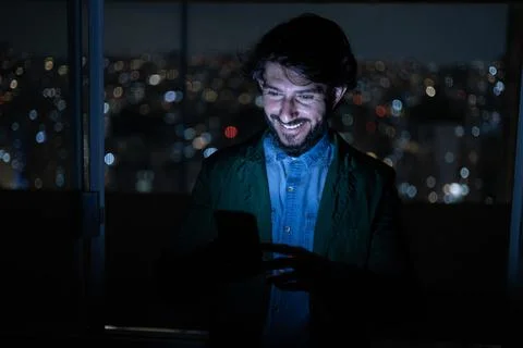 Front view of young man using a smartphone at night time with city view lands Stock Photos