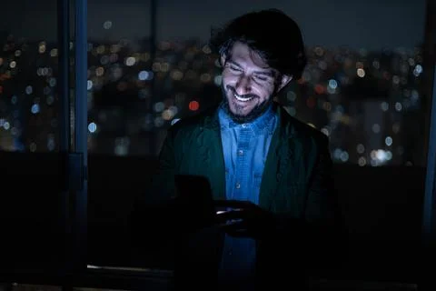 Front view of young man using a smartphone at night time with city view lands Stock Photos