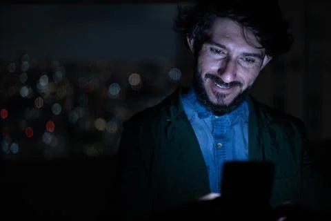 Front view of young man using a smartphone at night time with city view lands Stock Photos