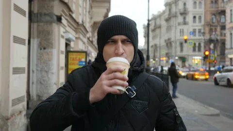 Front view of young man walking down the city street and drinking coffee.  Stock Footage 104833864