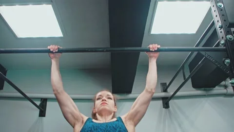 Front view of a young sportswoman pulls herself up on a horizontal bar in a gym. Stock Footage 153418475