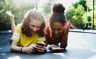 Front View Of Young Teenager Girls Friends Outdoors In Garden, Using Smartphone. Stock Photos