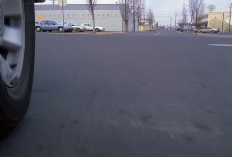 Front-wheel mount POV of car making a left turn and traveling on quiet street Stock Footage 86885402