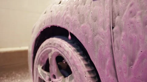 Front wing of a car and a wheel with pink foam dripping from it in car wash bay 库存影片 316415513