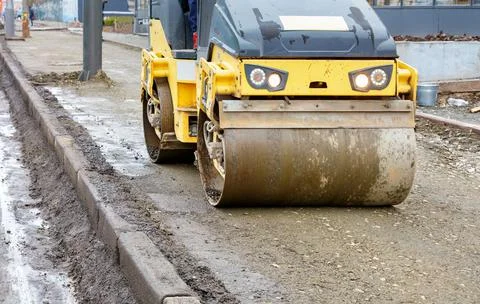 Frontal view of a road roller rolling the base of the sidewalk along a concre Stock Photos