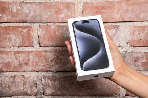 Frontview of the Iphone 15 Pro in a box in the hand on a red brick background Stock Photos