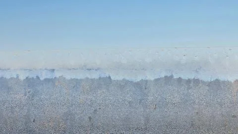 Frost blankets a window, creating delicate patterns that reflect the shimmeri Stock Photos