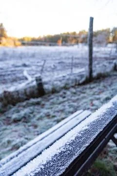 Frost-covered bench in the foreground with a blurred animal fence behind it Stock Photos