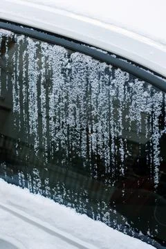 Frost patterns on a car window with snow covering the windshield during winter Stock Photos