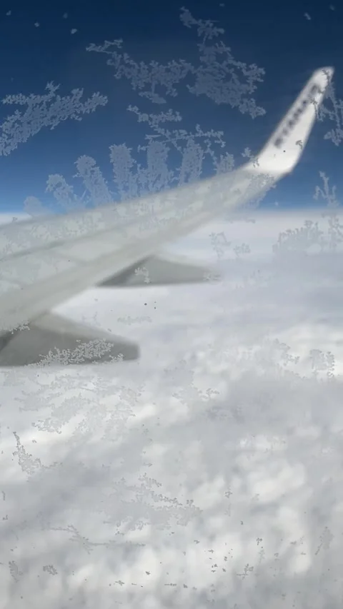 Frosted airplane window frames wing over vast sea clouds Stock Footage 310182940