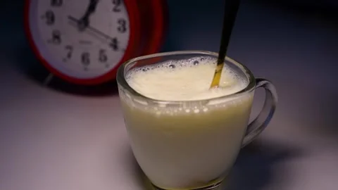 Frothy milk in a glass next to a clock, Glass of frothy milk with a golden .. Stock Footage 321937075