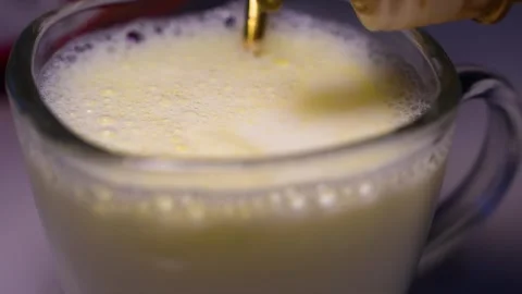 Frothy milk with golden liquid dropper, Close-up of a glass mug filled with.. Stock Footage 321937060