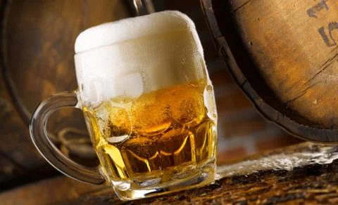 Frothy mug of beer set in a rustic cellar Stock Photos