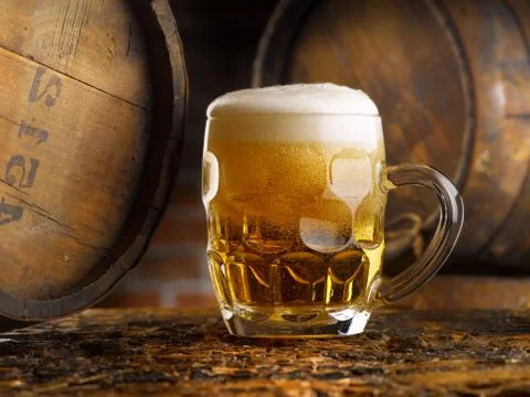 Frothy mug of beer set in a rustic cellar Stock Photos