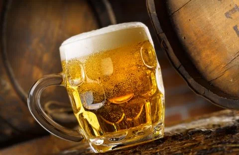 Frothy mug of beer set in a rustic cellar Stock Photos