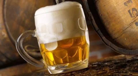 Frothy mug of beer set in a rustic cellar Stock Photos