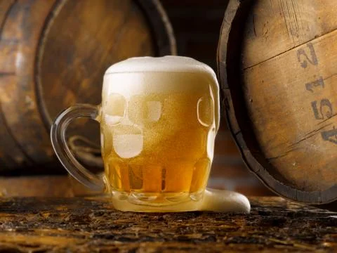 Frothy mug of beer set in a rustic cellar Stock Photos