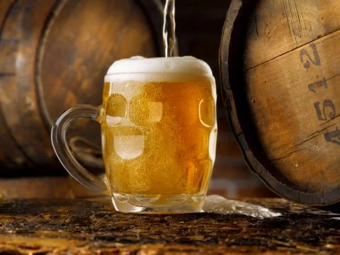 Frothy mug of beer set in a rustic cellar Stock Photos