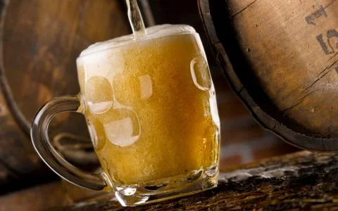 Frothy mug of beer set in a rustic cellar Stock Photos