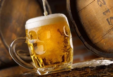 Frothy mug of beer set in a rustic cellar Stock Photos