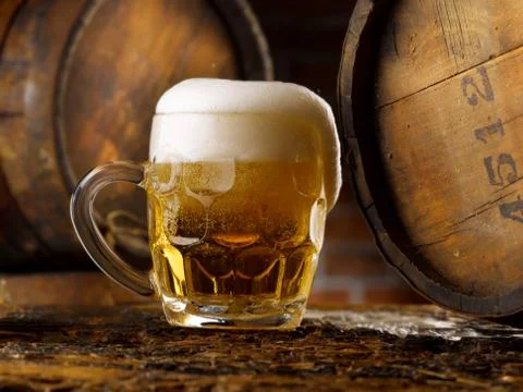 Frothy mug of beer set in a rustic cellar Stock Photos