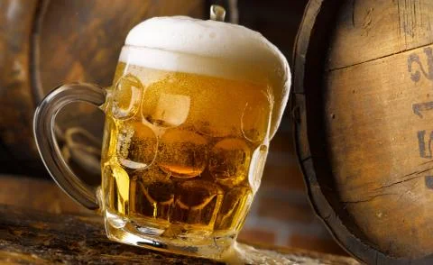 Frothy mug of beer set in a rustic cellar Stock Photos