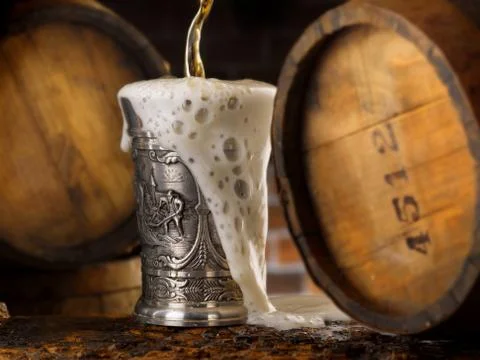 Frothy mug of beer set in a rustic cellar Stock Photos