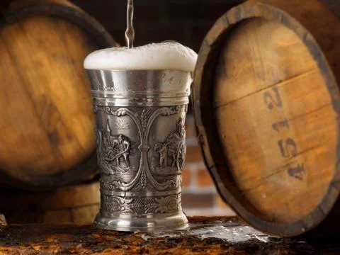 Frothy mug of beer set in a rustic cellar Stock Photos