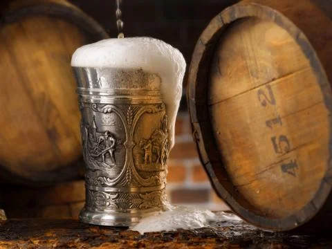Frothy mug of beer set in a rustic cellar Stock Photos