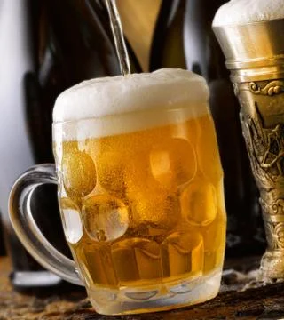 Frothy mug of beer set in a rustic cellar Stock Photos