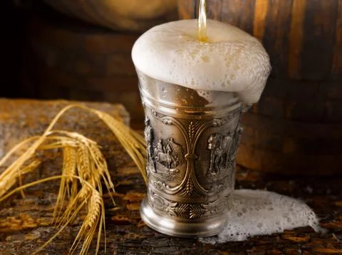 Frothy mug of beer set in a rustic cellar Stock Photos