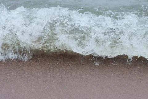 Frothy wave rolls to shore. Stock Photos