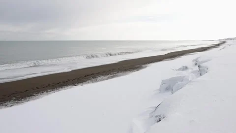 Frothy waves breaking on snow-covered winter beach on bright morning Stock Footage 303256508
