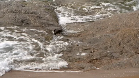Frothy Waves Flow Over Large Brown Rocks on a Beach in Paros Stock Footage 101205770