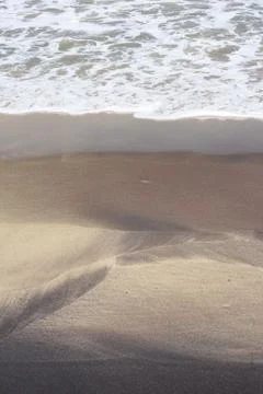 Frothy waves form pattern on beach sand Stock Photos