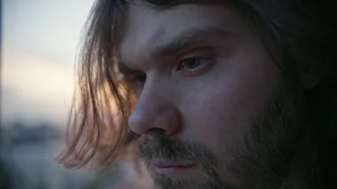 Frown, serious man with beard and long hair looking around outside, sunset city Stock Footage 246456595